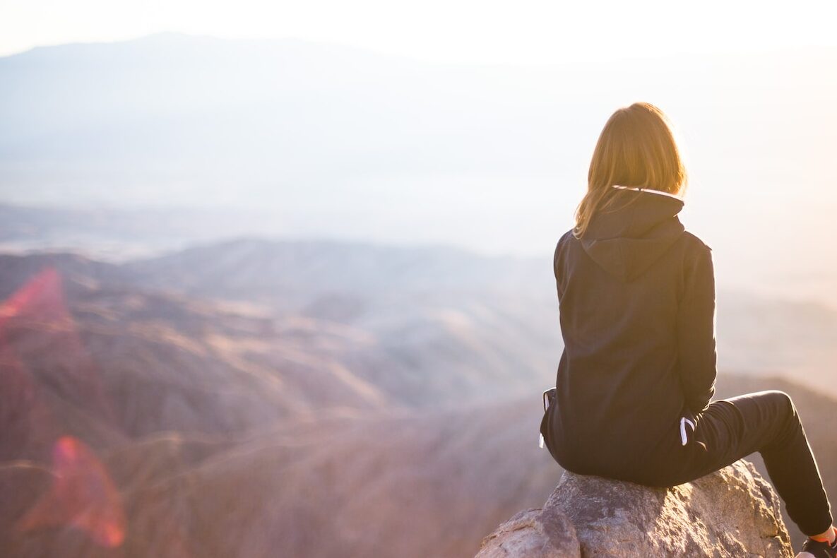 person sitting on top of gray rock overlooking mountain during daytime